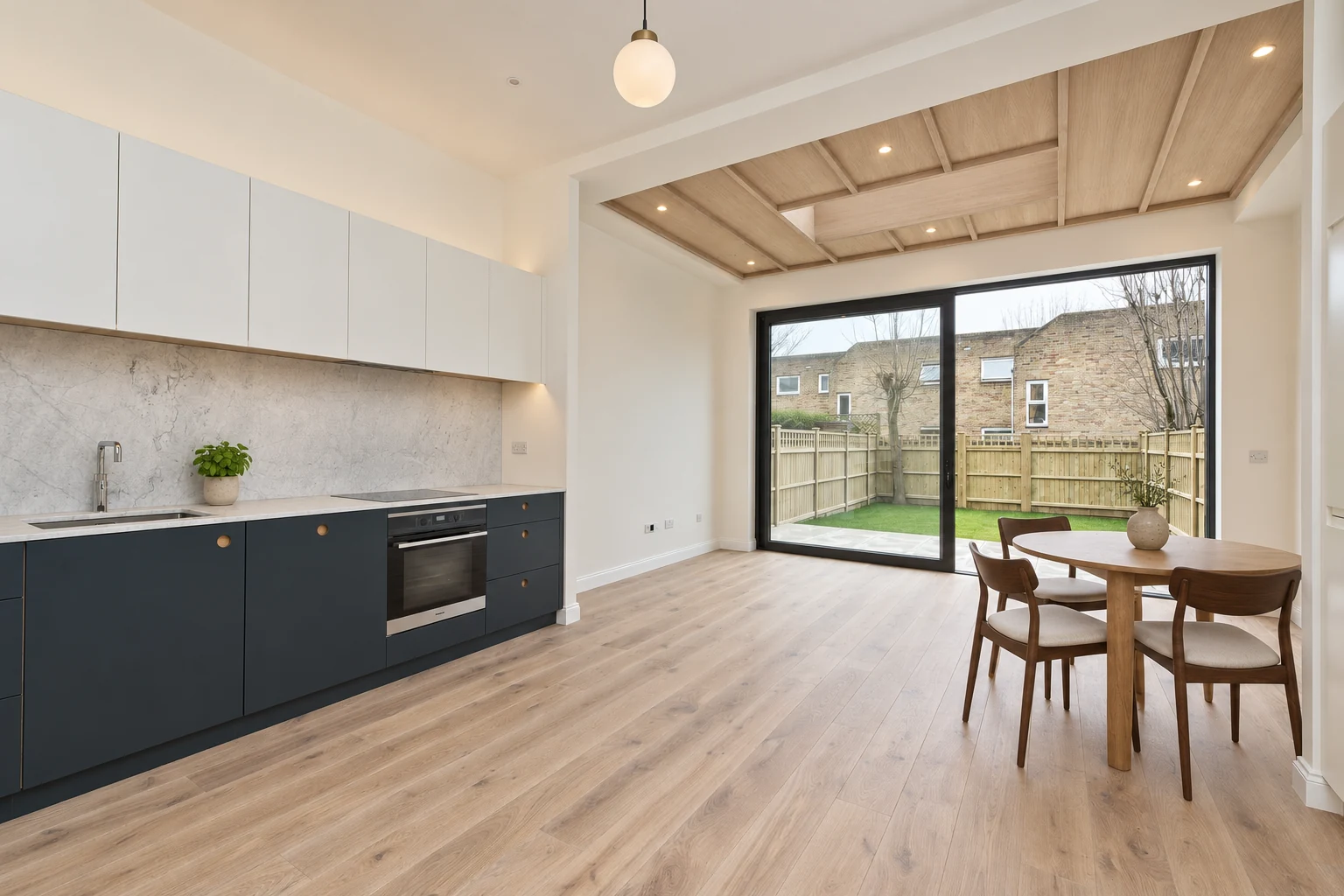 Dark blue kitchen cabinets, a coffered timber ceiling and round dining table beside garden glazing.