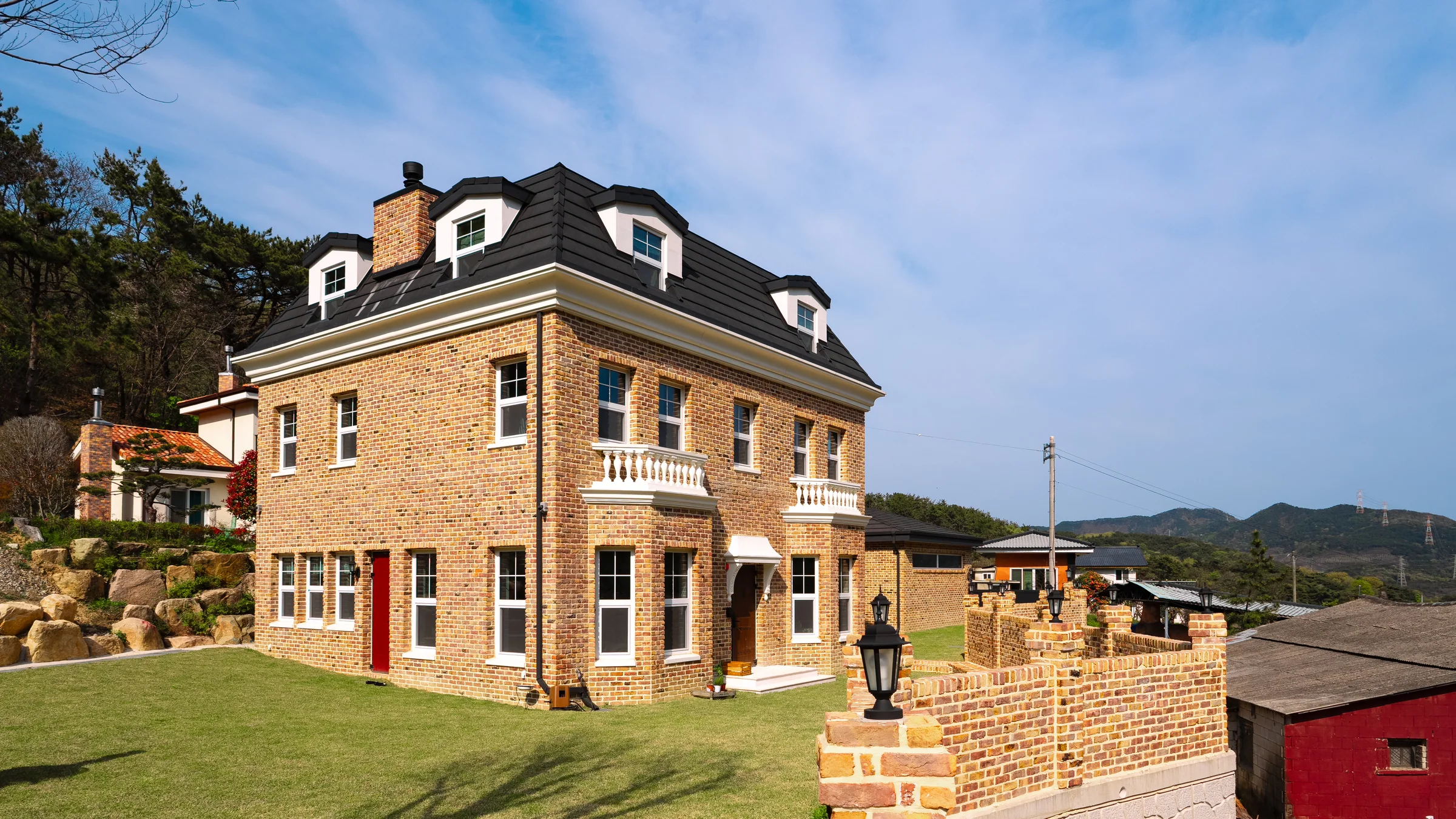 Gaju House and its garden, with brick walls, tall windows and a mansard roof.