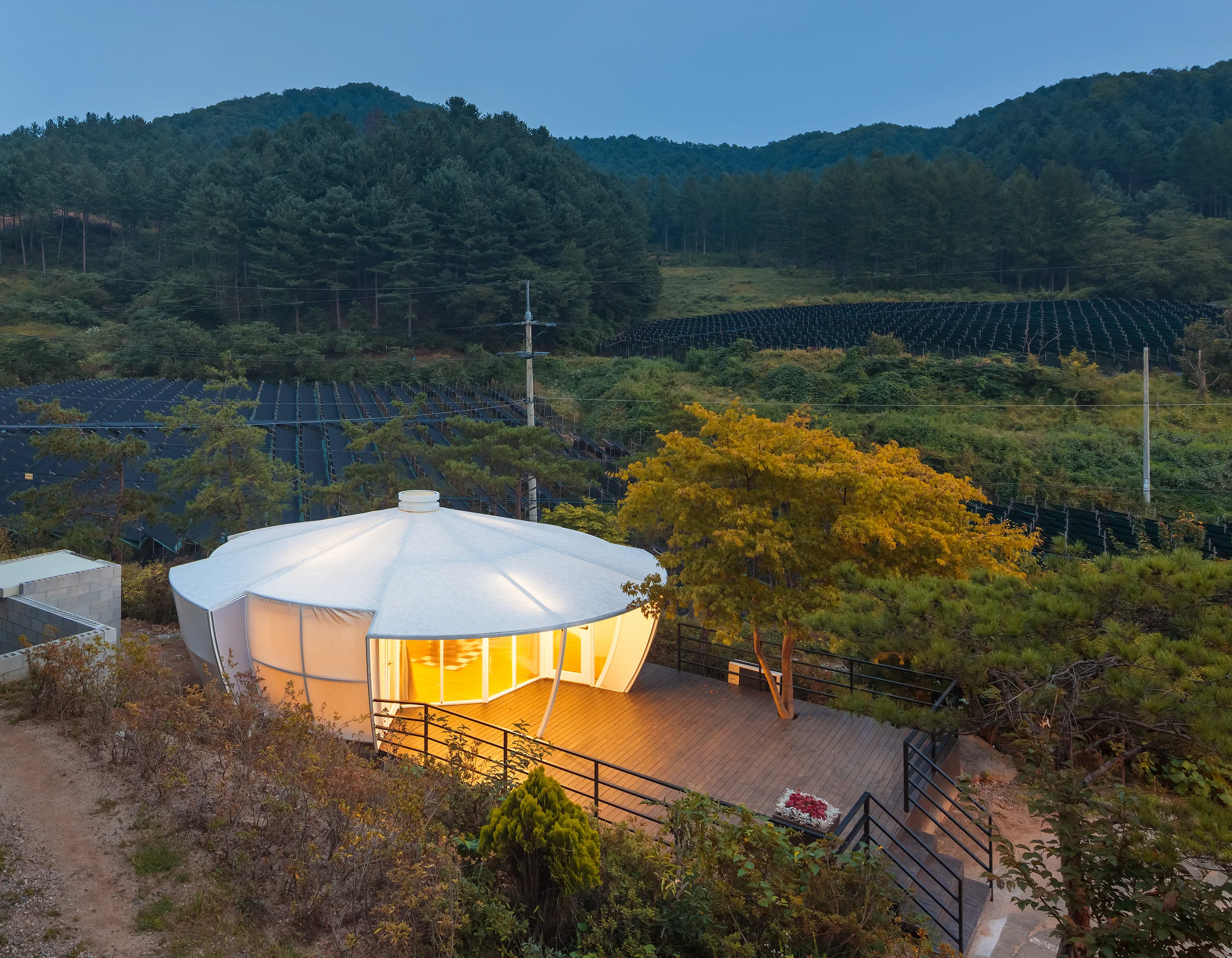 Illuminated glamping pavilion set within a wooded landscape at dusk.