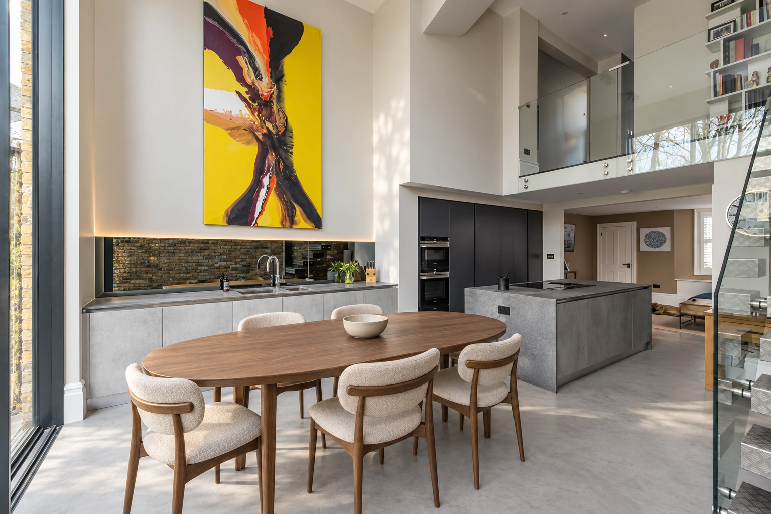 Double-height dining space, walnut table and concrete kitchen beneath the mezzanine at Kingston Road.