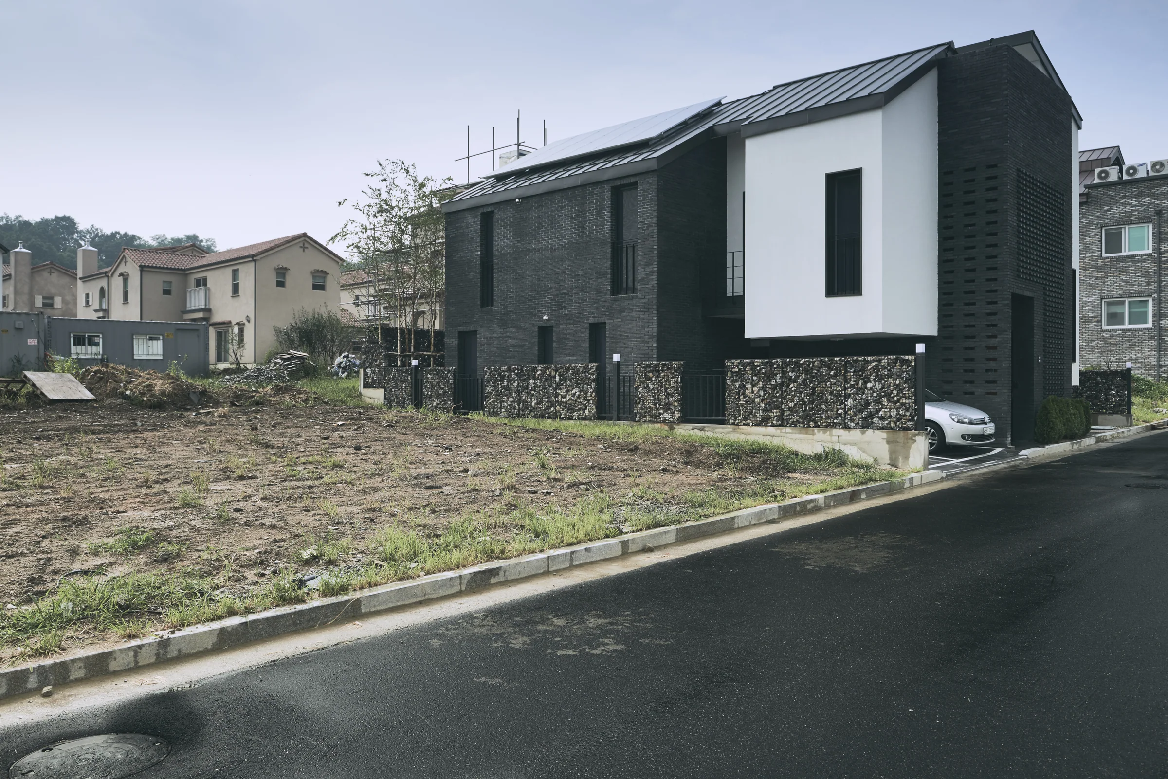 Oblique exterior view of Layer House with dark brickwork and white upper walls.