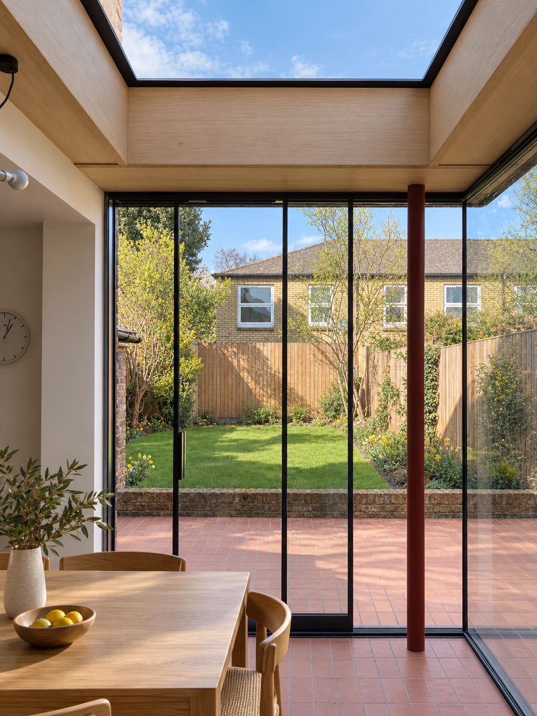 Garden room with a deep timber rooflight, terracotta floor, dark-framed glazing and a burgundy corner column.