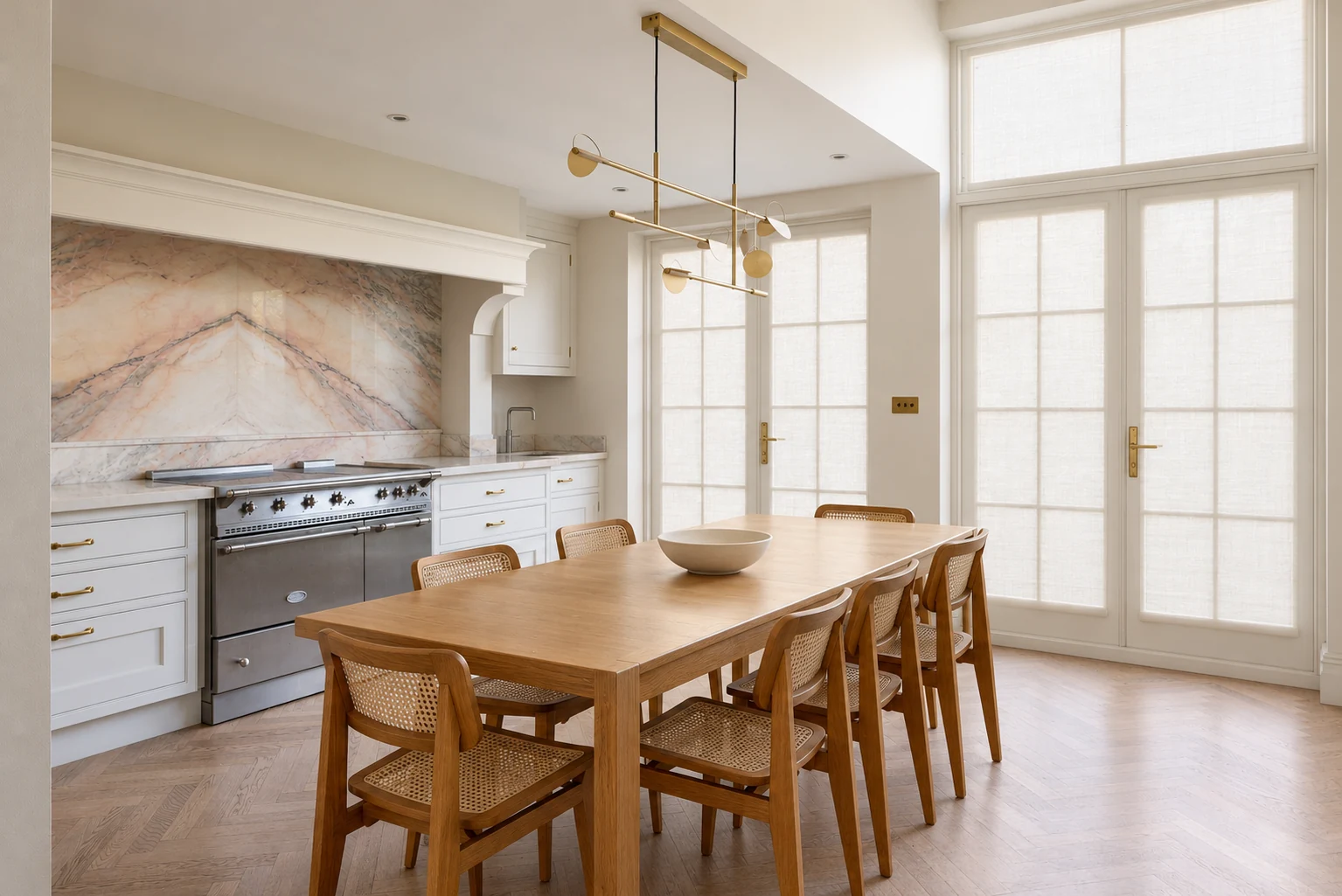Kitchen with a veined stone cooker recess, white panelled cupboards, tall French doors and herringbone floor.